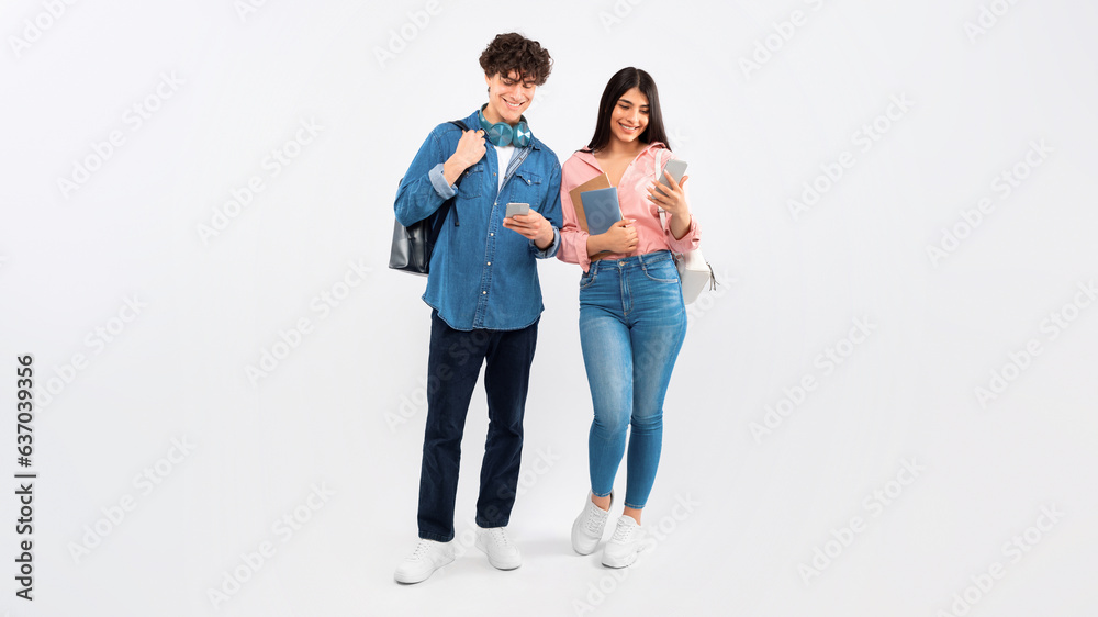 Cheerful Young Students Couple Using Phones On White Studio Background