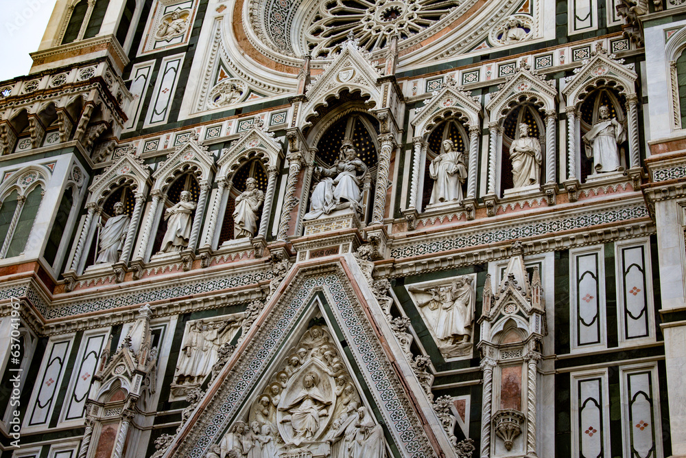 A close-up of Florence Cathedral reveals the sculptural elegance of its facade, where marble statues stand in harmony with ornate Gothic detailing under an Italian sky.