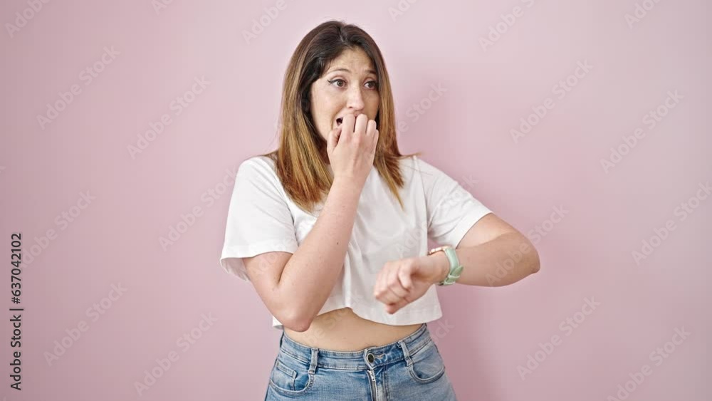 Young blonde woman looking watch with nervous expression over isolated pink background Young blonde woman looking watch with nervous expression over isolated pink background