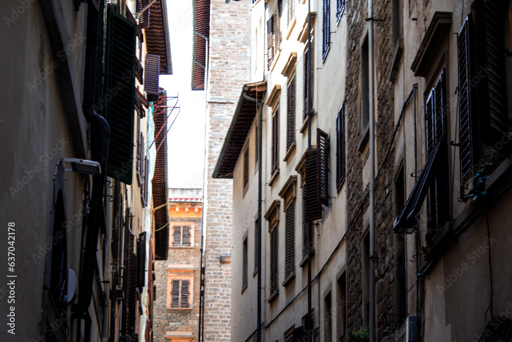 A narrow alley in Florence offers a perspective of urban life, with windows adorned with shutters and the textured walls of storied buildings inviting exploration and discovery.