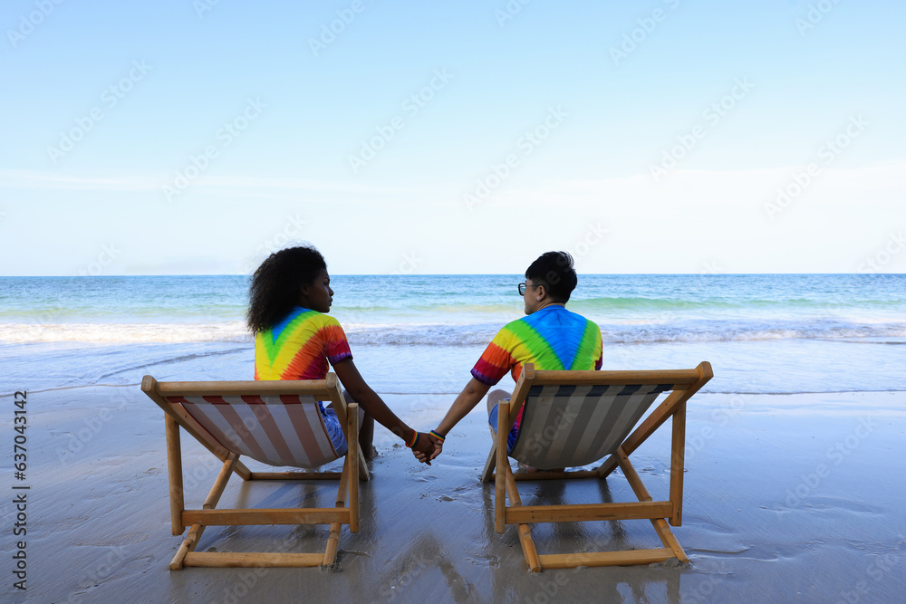They are a lovely LGBTQ  couple hand to hand relaxing on the beach. two females lying on the sun bed  at the beach