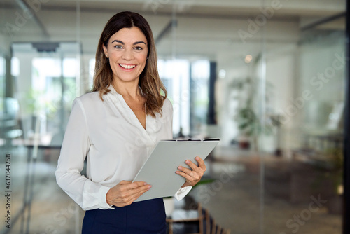 Happy 45 years old Latin professional middle aged business woman corporate leader, happy mature female executive, lady manager standing in office holding clipboard looking at camera, portrait. photo