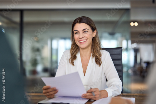 Smiling mature business woman hr holding cv at job interview. Happy mid aged professional banking financial manager, insurance agent, lawyer consulting clients sitting at work corporate office meeting