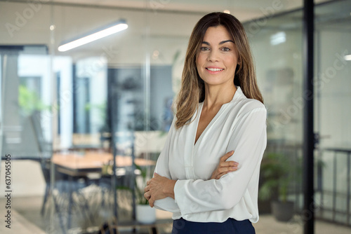Smiling confident 45 years old Latin professional middle aged business woman corporate leader, happy mature female executive, lady manager standing in office arms crossed looking at camera, portrait.