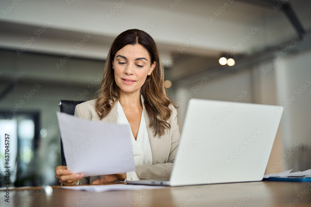 Busy 40 years old business woman working in office checking documents. Mid aged businesswoman accounting manager executive or lawyer using laptop reading paper file financial report, tax invoice. Busy 40 years old business woman working in office checking documents. Mid aged businesswoman accounting manager executive or lawyer using laptop reading paper file financial report, tax invoice.