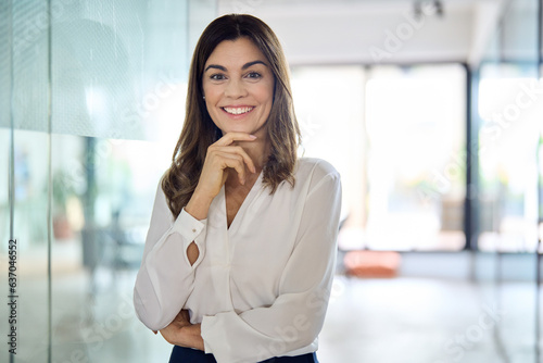 Happy confident Latin professional mid aged business woman in office, portrait. Smiling lady corporate leader, mature female executive, lady manager standing in looking at camera, portrait. photo