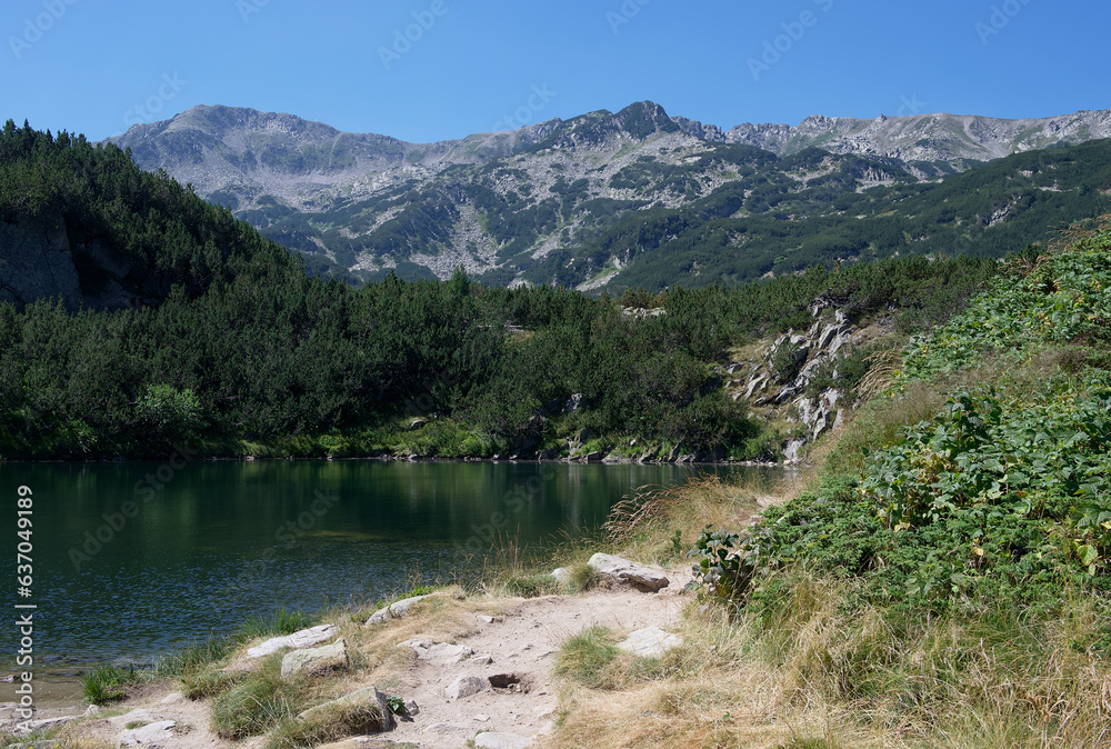 A calm mountain lake among the surrounding mountain peaks is covered by the bright rays of the sun.