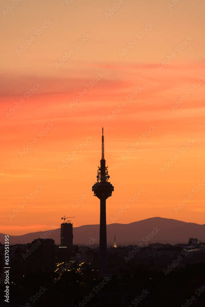 Silhouettes of buildings of a city, highlighting the silhouette of a communications tower with an orange sky with clouds at sunset