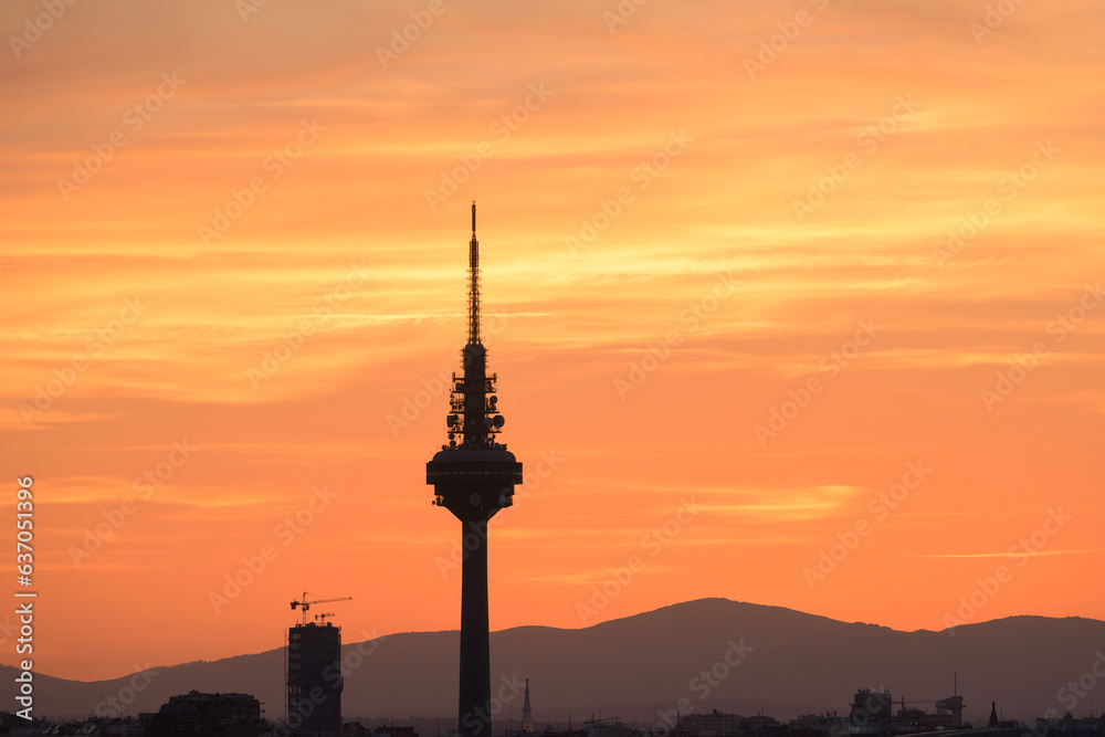 Silhouettes of buildings of a city, highlighting the silhouette of a communications tower with an orange sky with clouds at sunset