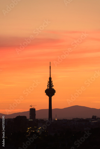 Silhouettes of buildings of a city  highlighting the silhouette of a communications tower with an orange sky with clouds at sunset