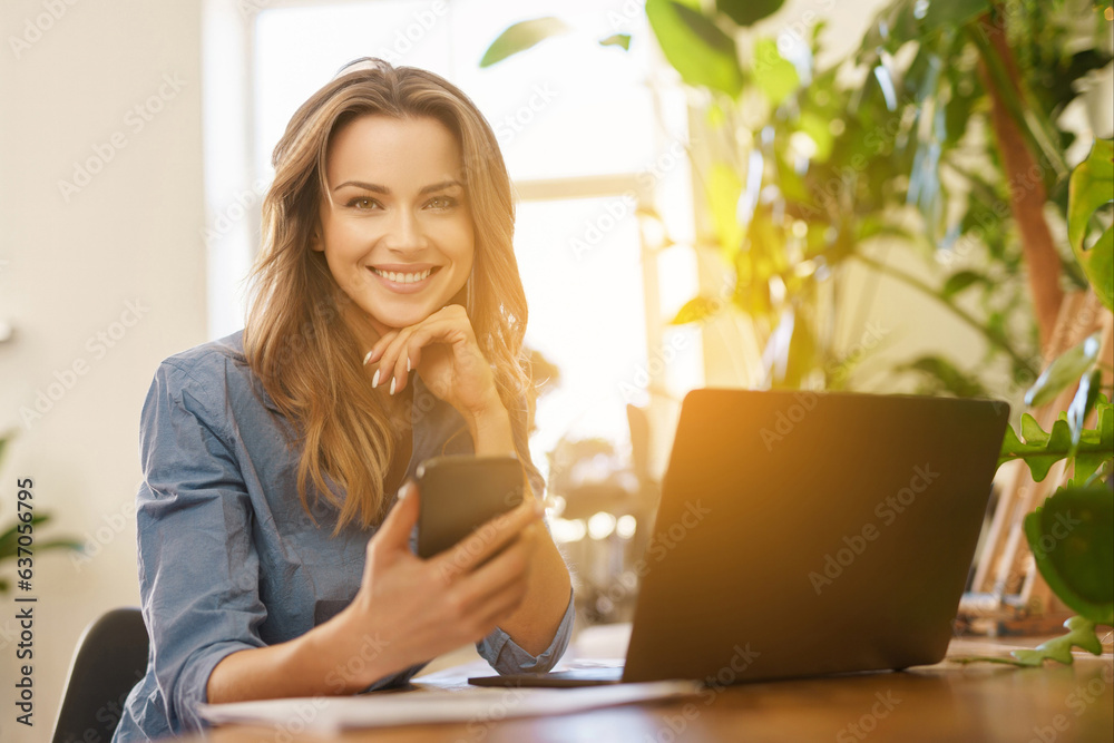 Beautiful smiling freelance woman in blue shirt working on laptop in a sunlit room filled with plants Beautiful smiling freelance woman in blue shirt working on laptop in a sunlit room filled with plants