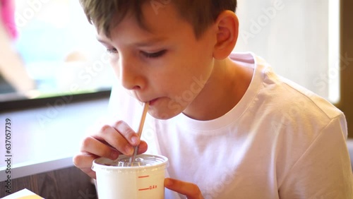 a ten-year-old boy drinks a cold drink through a straw while sitting at the table. going to a cafe.