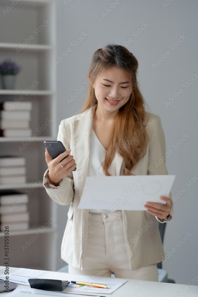 Portrait of a smiling asian businesswoman using mobile phone and holding document in the office. Portrait of a smiling asian businesswoman using mobile phone and holding document in the office.