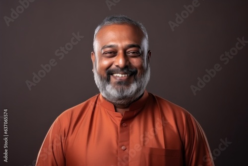 Medium shot portrait of an Indian man in his 50s against a minimalist or empty room background wearing hijab