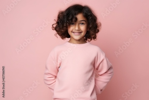 Medium shot portrait of an Indian child female against a pastel or soft colors background wearing a cozy sweater