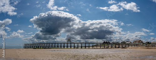 Luc-Sur-Mer, France, France - 07 26 2023:  View of a cloudy rainy sky, the wooden Fisherman's Pier, the seawall, beach cabins and people above the sea from the beach. photo