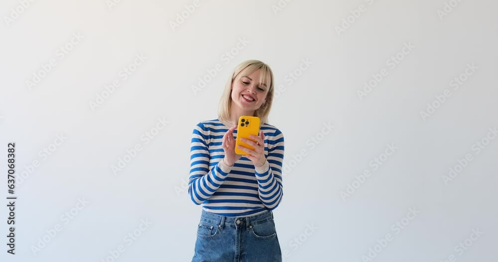 A woman is seen on a clean white backdrop, happily browsing on her phone and bursting into laughter. Her radiant smile and joyous laughter indicate her delight in the content she is viewing. A woman is seen on a clean white backdrop, happily browsing on her phone and bursting into laughter. Her radiant smile and joyous laughter indicate her delight in the content she is viewing.