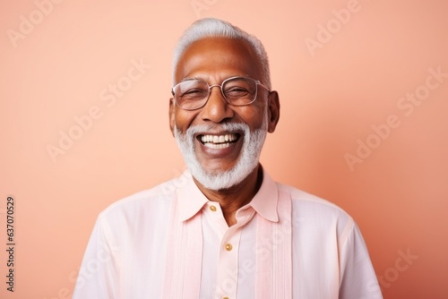 Portrait of a senior Indian man wearing glasses and smiling while standing against pink background