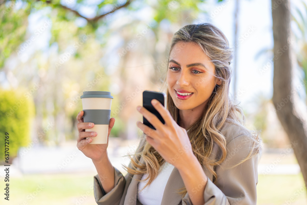Young pretty blonde Uruguayan woman at outdoors using mobile phone and holding a take away coffee Young pretty blonde Uruguayan woman at outdoors using mobile phone and holding a take away coffee
