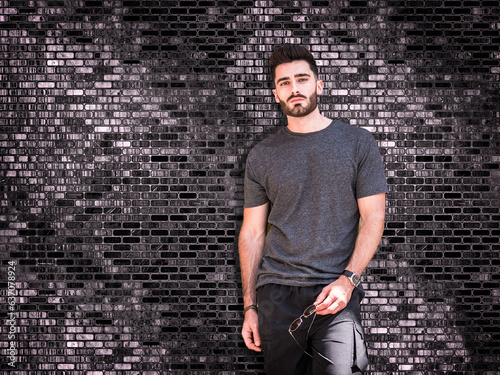 Photo of a man standing in front of a textured brick wall