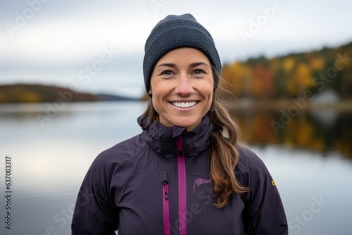 Portrait of a smiling young woman wearing warm sportswear and cap standing by a lake in autumn photo