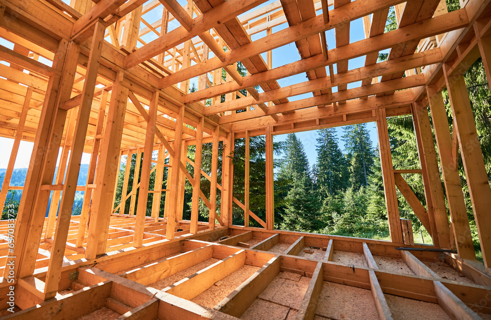 Under-construction residential wooden frame home located near a forest. Commencement of a new construction project for a cozy house or a mountain cottage. Idea of contemporary ecological construction. Under-construction residential wooden frame home located near a forest. Commencement of a new construction project for a cozy house or a mountain cottage. Idea of contemporary ecological construction.