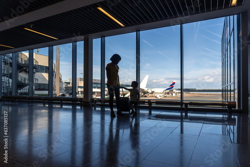 Silhouette of mother and son with luggage near the window in the airport looking at planes before flying