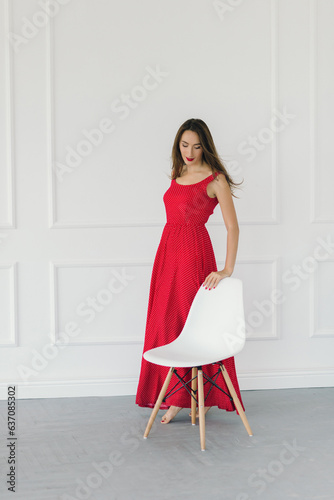 beautiful sexy girl in a red dress posing on the background of a wall in a photo studio