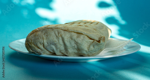 Large shawarma on a white plate with a napkin on a blue background with shadows. Food, healthy fast food, delicious to eat.
