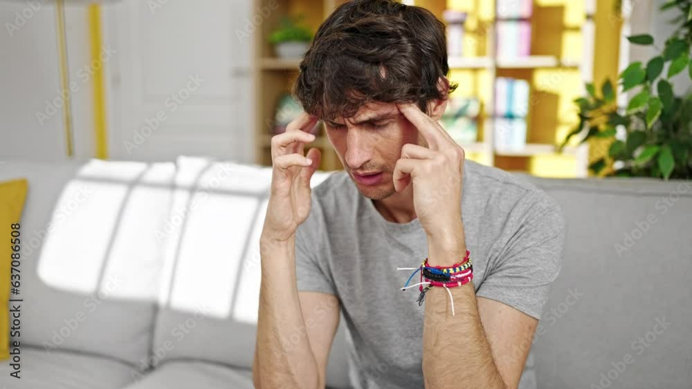 Young hispanic man suffering for headache sitting on sofa at home Young hispanic man suffering for headache sitting on sofa at home