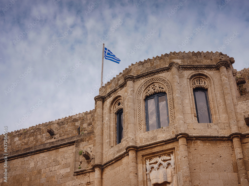 facade of an old beautiful building with the national Greek flag in sunset time. Travel to Greece, Mediterranean islands Rhodes.