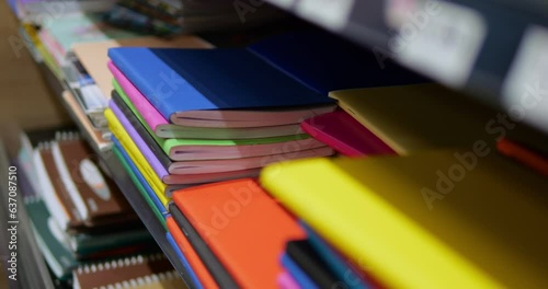 Close-up of stack of multicolored notebooks and exercise books on shelf in shop. Heap of composition books of solid vibrant colors lie for sale in store. photo