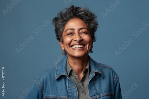 Medium shot portrait of an Indian woman in her 50s wearing a denim jacket in a minimalist background