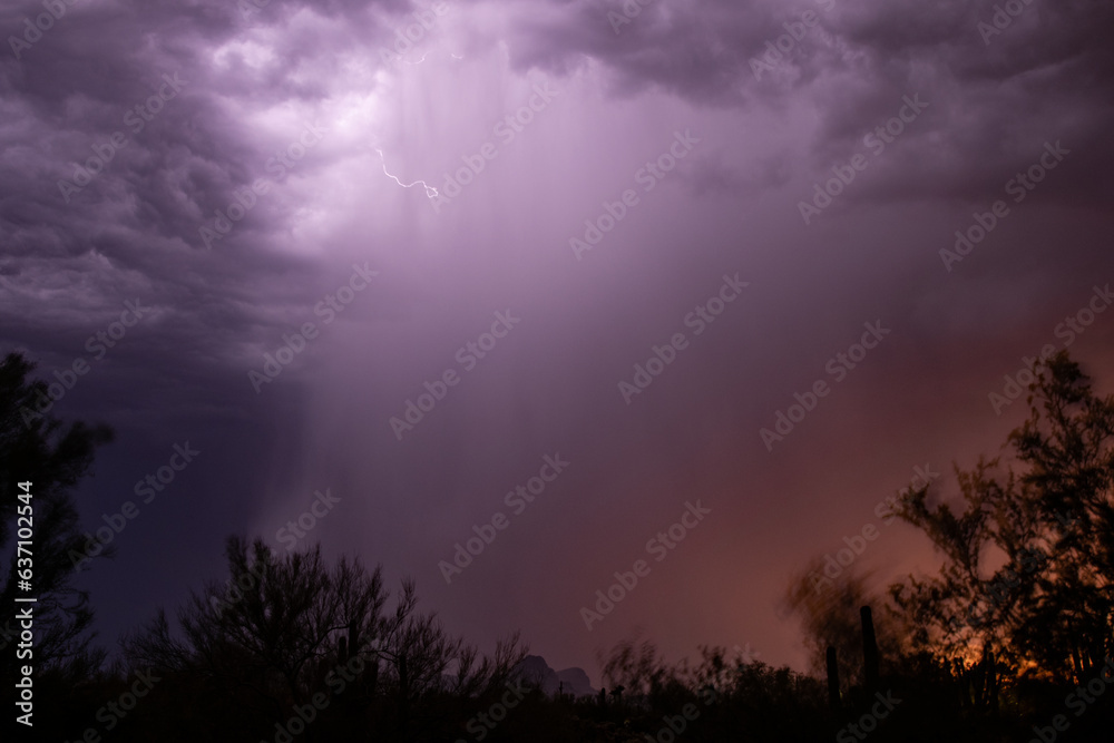 A rain shaft at sunset is illuminated by lightning in the desert
