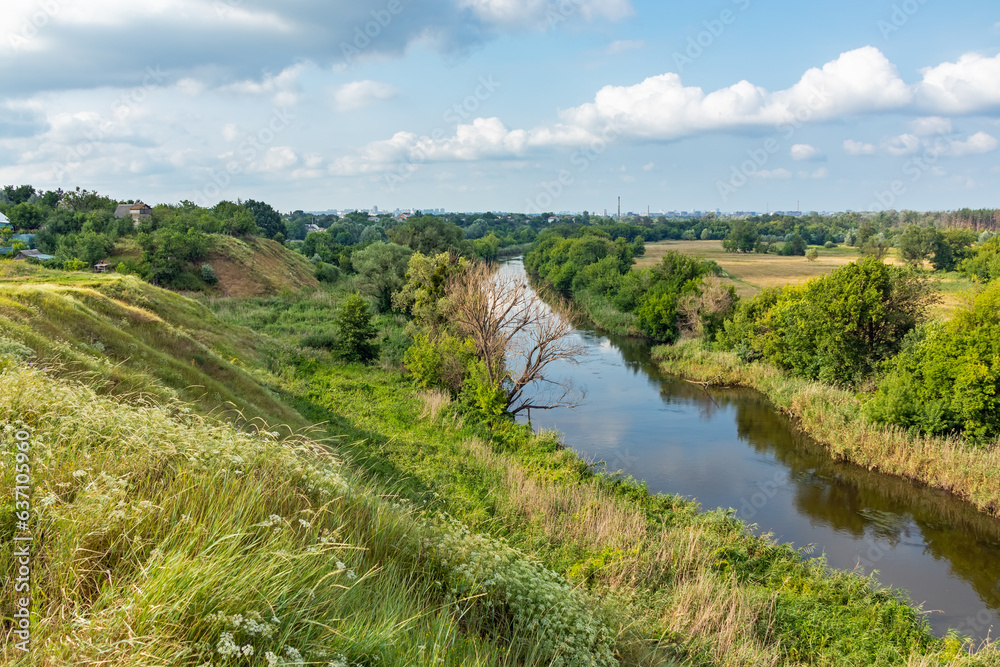 View from the hill to the river valley with trees and a meadow on a summer sunny day. Outskirts of Kharkiv city, Ukraine