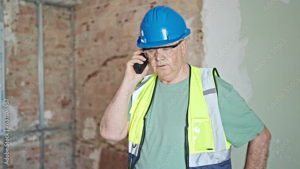 Middle age grey-haired man architect talking on walkie-talkie at construction site Middle age grey-haired man architect talking on walkie-talkie at construction site