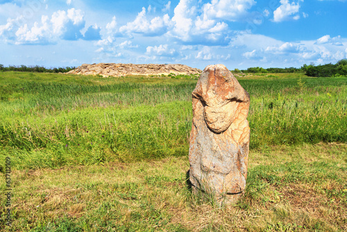 View of the ancient kurgan stela, stone idol against the backdrop of ancient mound of sandstone boulders, in the archeological preserve Kamyana Mohyla, Ukraine photo
