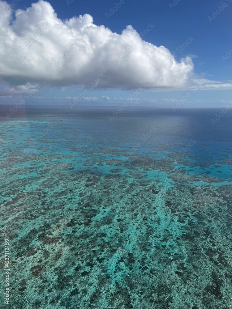 Vibrant Great Barrier Reef with bright blue water and wispy white clouds in the background