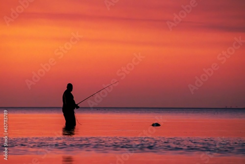 Silhouette of a man fishing at a stunning sunset