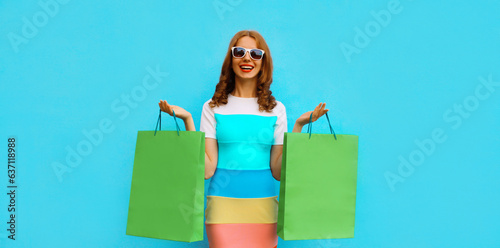 Beautiful happy smiling young woman posing with shopping bags on blue studio background