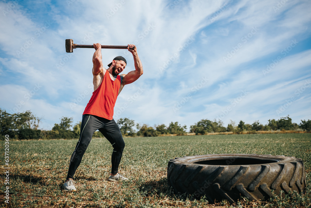 Incredible Strength Muscular Man Demonstrating Power, Hitting Rubber Tire with Hammer at Cross fit Training Outdoors. Muscular Man Power Hitting Rubber Tire with Hammer at Cross fit Training Outdoors