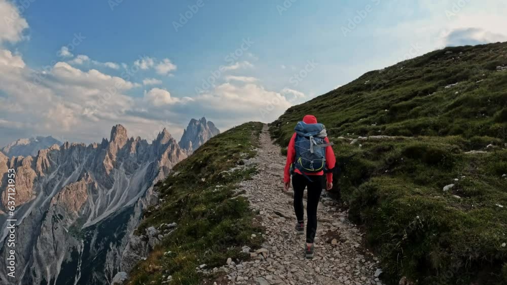 Active woman with backpack hiking trail path and climbing Dolomites mountain. Summer adventure journey in nature outdoors. Travel exploring Alps, Dolomites, Italy Active woman with backpack hiking trail path and climbing Dolomites mountain. Summer adventure journey in nature outdoors. Travel exploring Alps, Dolomites, Italy
