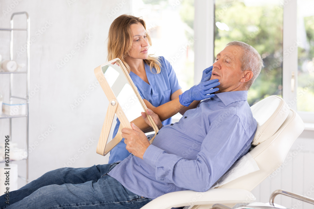 Obraz premium Old male patient lying on clinical chair discussing face aesthetic procedures with doctor