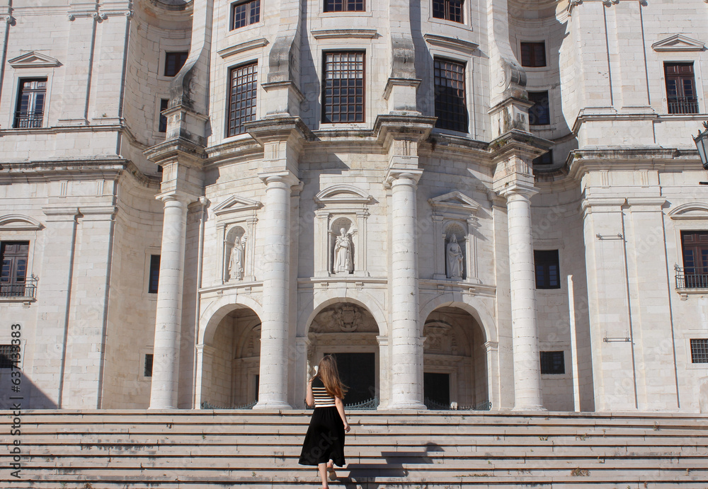 Young adult woman walking up the stairs in front of a huge building.