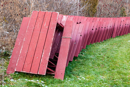 Red picnic tables stacked for winter storage in park.