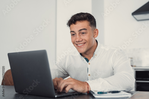 Side view handsome young businessman in eyewear working with computer remotely, sitting at wooden table in office. Pleasant happy man communicating in social network, searching information online..