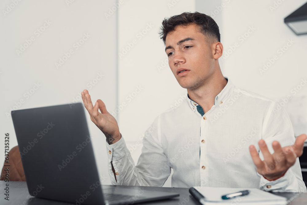 Unhappy young caucasian male worker in glasses look at laptop screen shocked by gadget breakdown or operational problems. Frustrated man confused surprised by unexpected error on computer device..