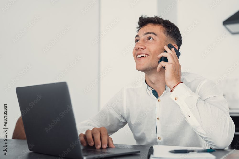 Smiling businessman wearing glasses talking on phone, sitting at desk with laptop, friendly manager consulting customer by phone, happy man chatting with friends distracted from work. Smiling businessman wearing glasses talking on phone, sitting at desk with laptop, friendly manager consulting customer by phone, happy man chatting with friends distracted from work.