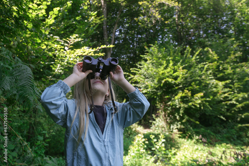 Fototapeta premium Cute little girl exploring nature looking through binoculars. Child playing outdoors. Kids travel, adventure and bird watching concept.