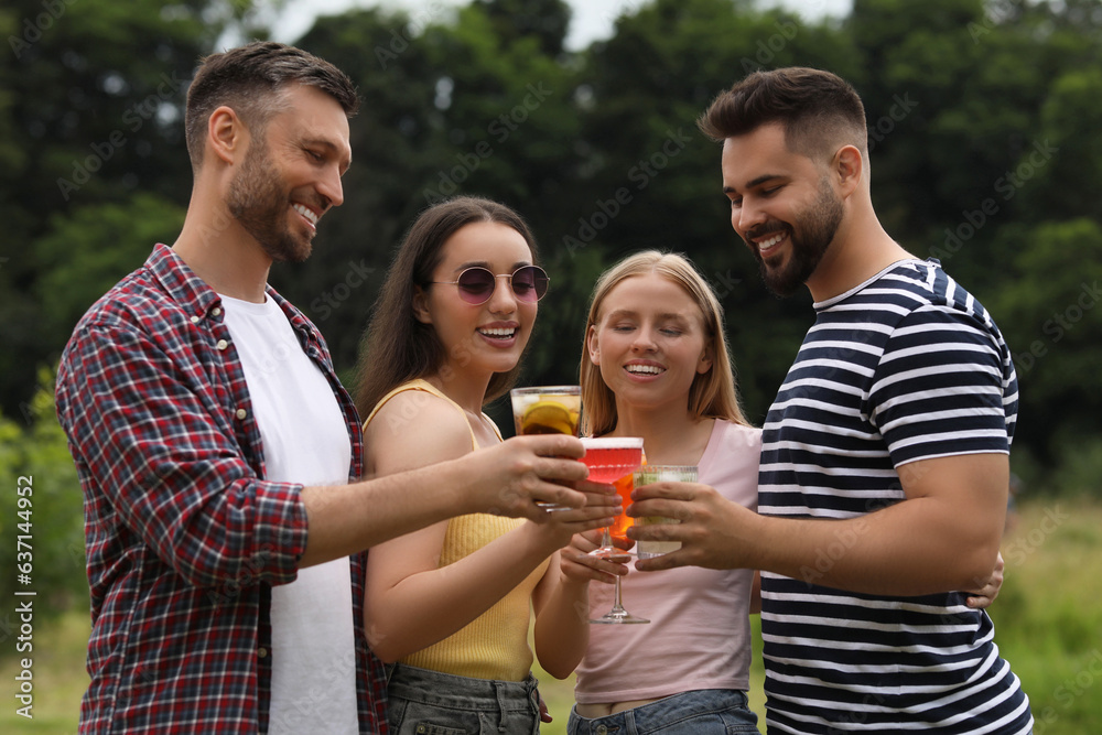 Obraz premium Happy friends clinking glasses with cocktails outdoors